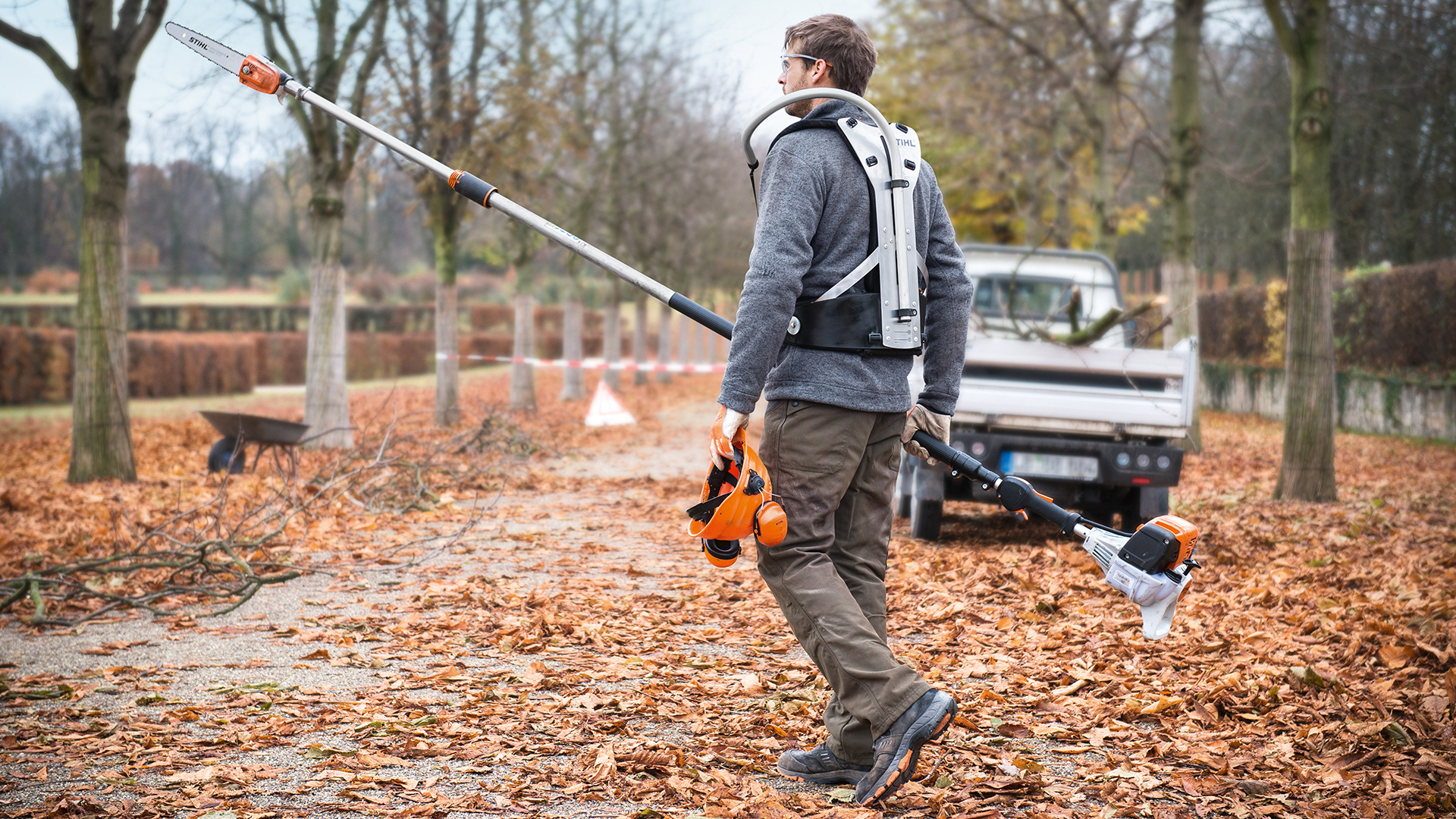 Man met STIHL HT 133 benzinehoogsnoeier en werkvoertuig in het park in de herfst