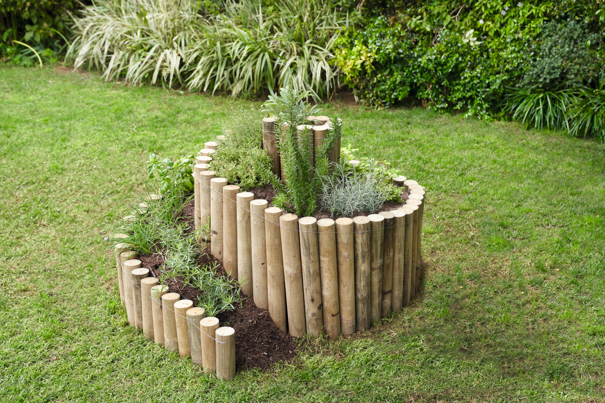 Kruidenspiraal met houten paaltjes op een stukje grond in de tuin