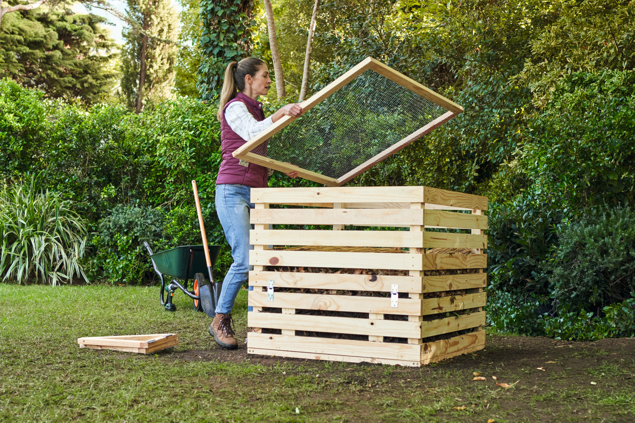 Vrouw dekt een zelfgemaakte compostbak af in een tuin