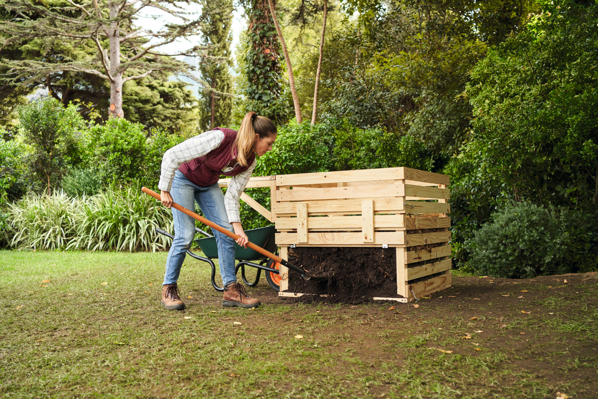 Een vrouw met een paardenstaart zet compost over met een schop