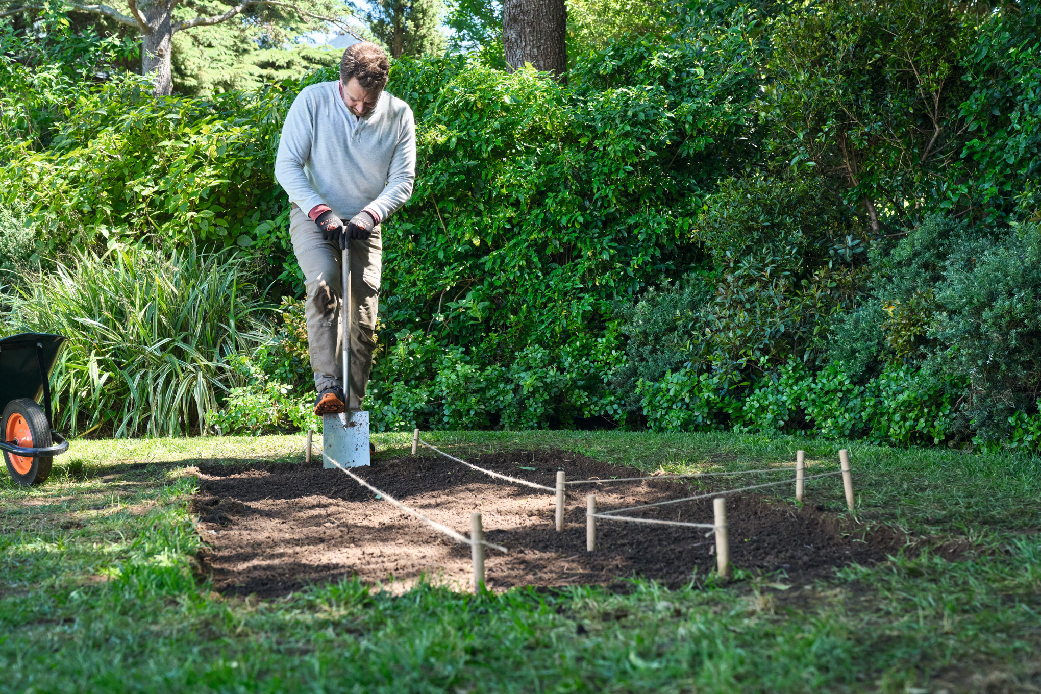 Een man met een spade in zijn hand graaft een uitgezet pad uit