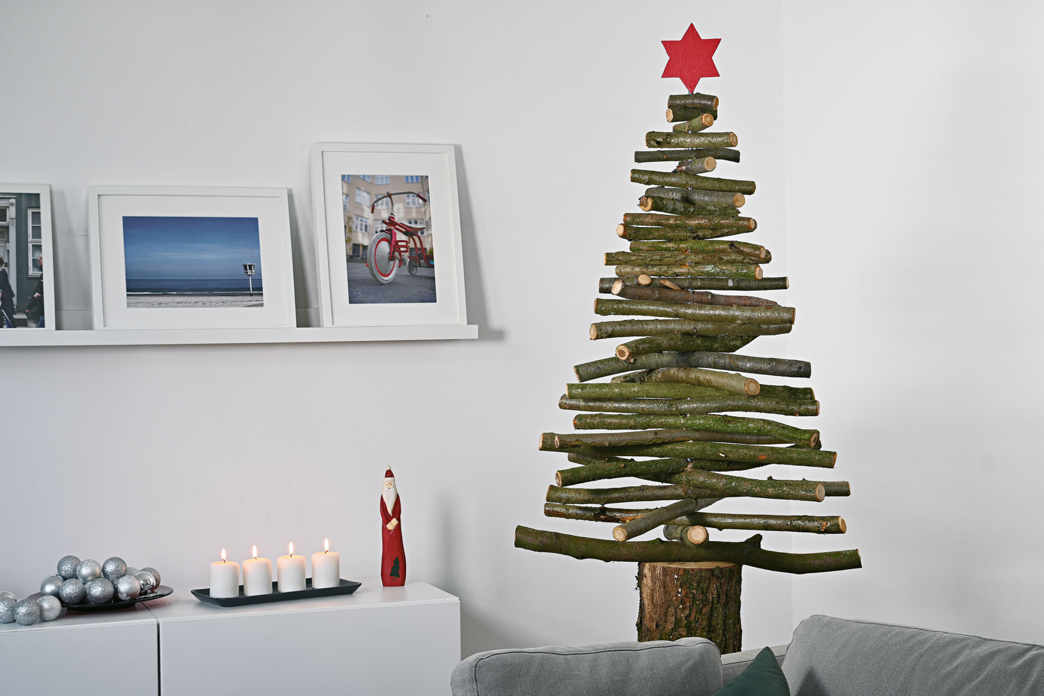 Een zelfgemaakte kerstboom van houten takken met een rode ster op de piek in een interieur in kerstsfeer