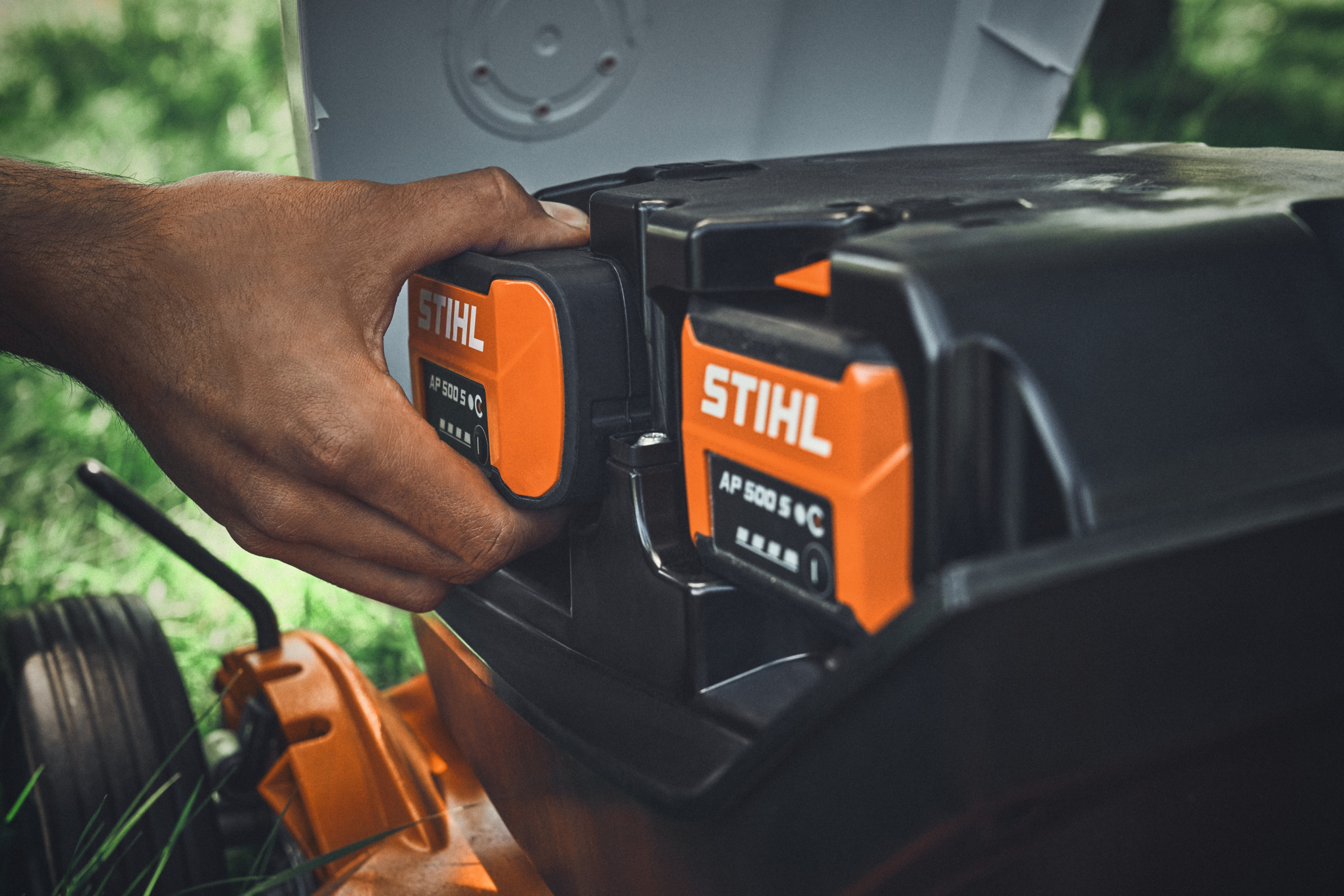 Iemand steekt een STIHL AP 500 S accu in een STIHL accugrasmaaier