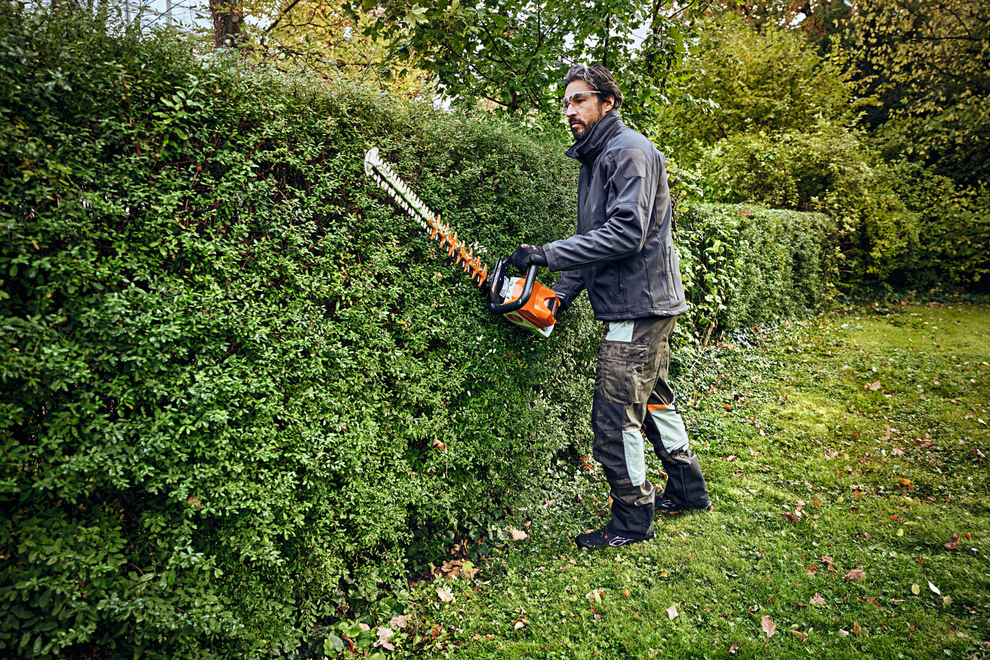 Een man in beschermende uitrusting snoeit een heg met een STIHL heggensnoeier 