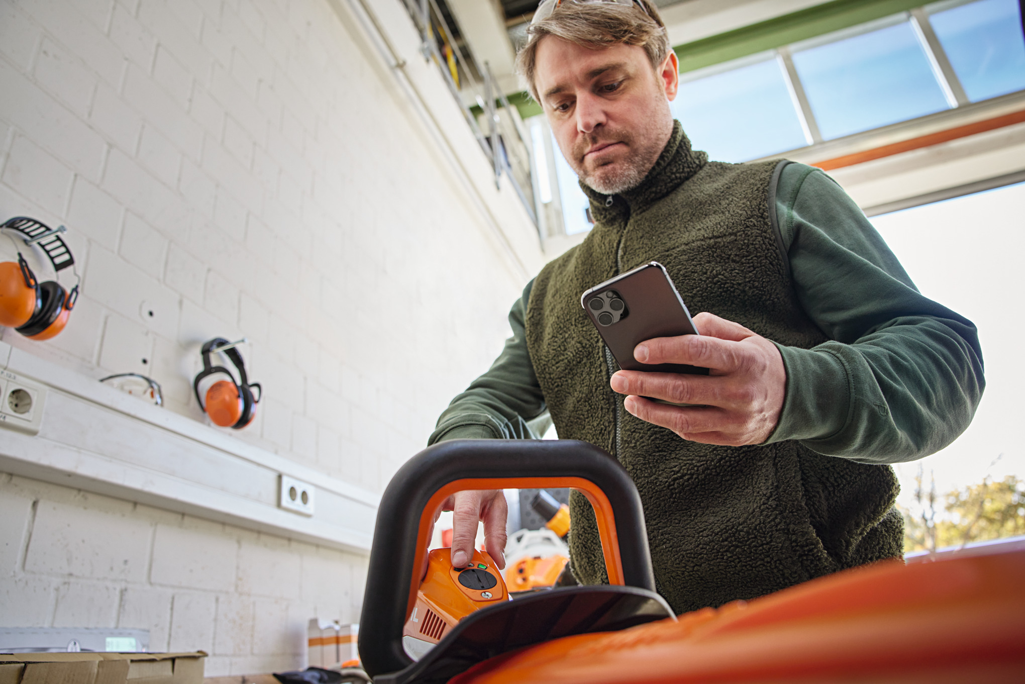 Iemand controleert de machinestatus op de Smart Connector 2 A en kijkt op zijn smartphone met de STIHL connected app