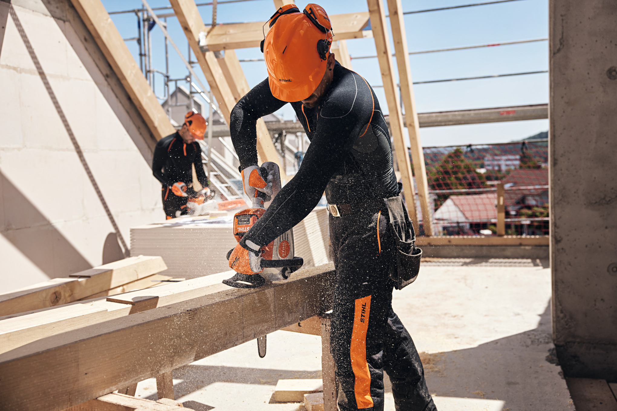 Een STIHL professional zaagt met een accukettingzaag een houten balk door, op de achtergrond werkt nog een arbeider met een accukettingzaag