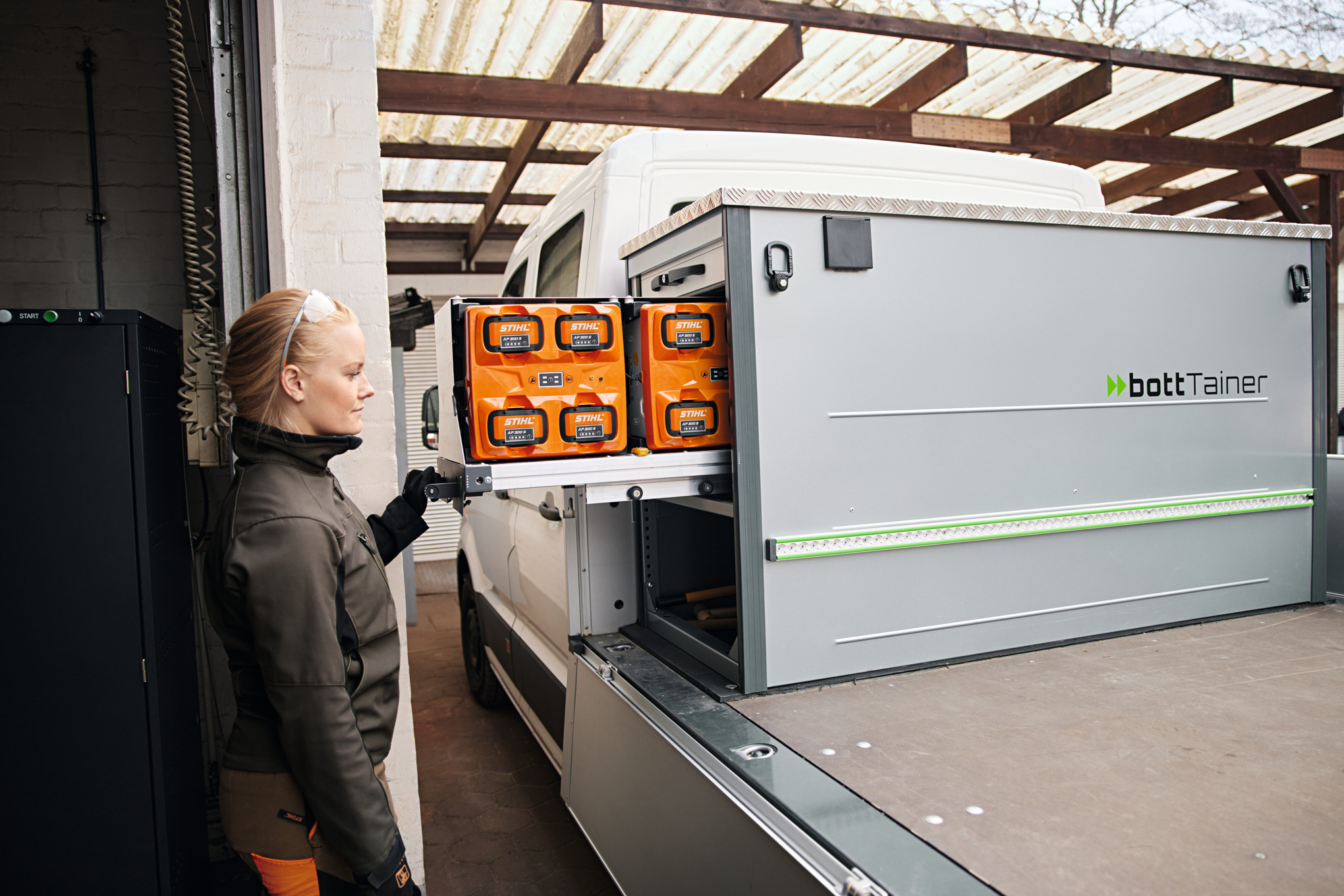 Blonde vrouw in zijprofiel naast een voertuig met laadvloer bij het hanteren van de accu's in de bottTainer