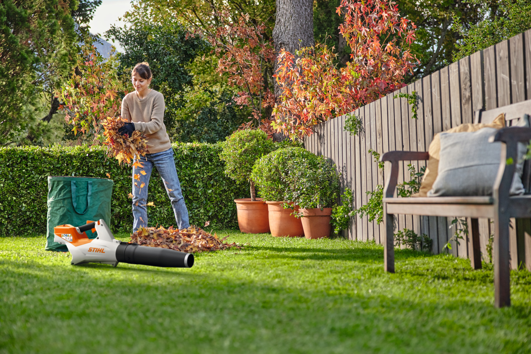 Een vrouw ruimt bladeren in een tuin op met een STIHL BGA 60 accubladblazer