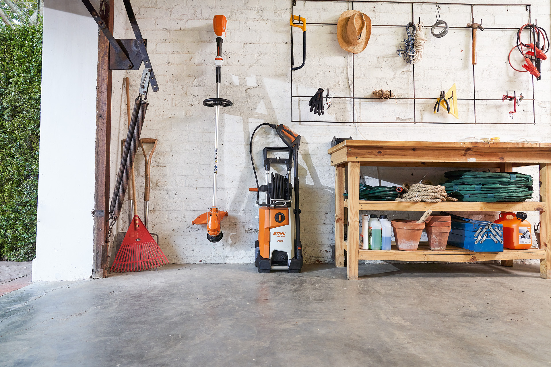 STIHL RE 130 plus hogedrukreiniger en een STIHL bosmaaier worden opgeborgen naast tuingereedschap in een garage 