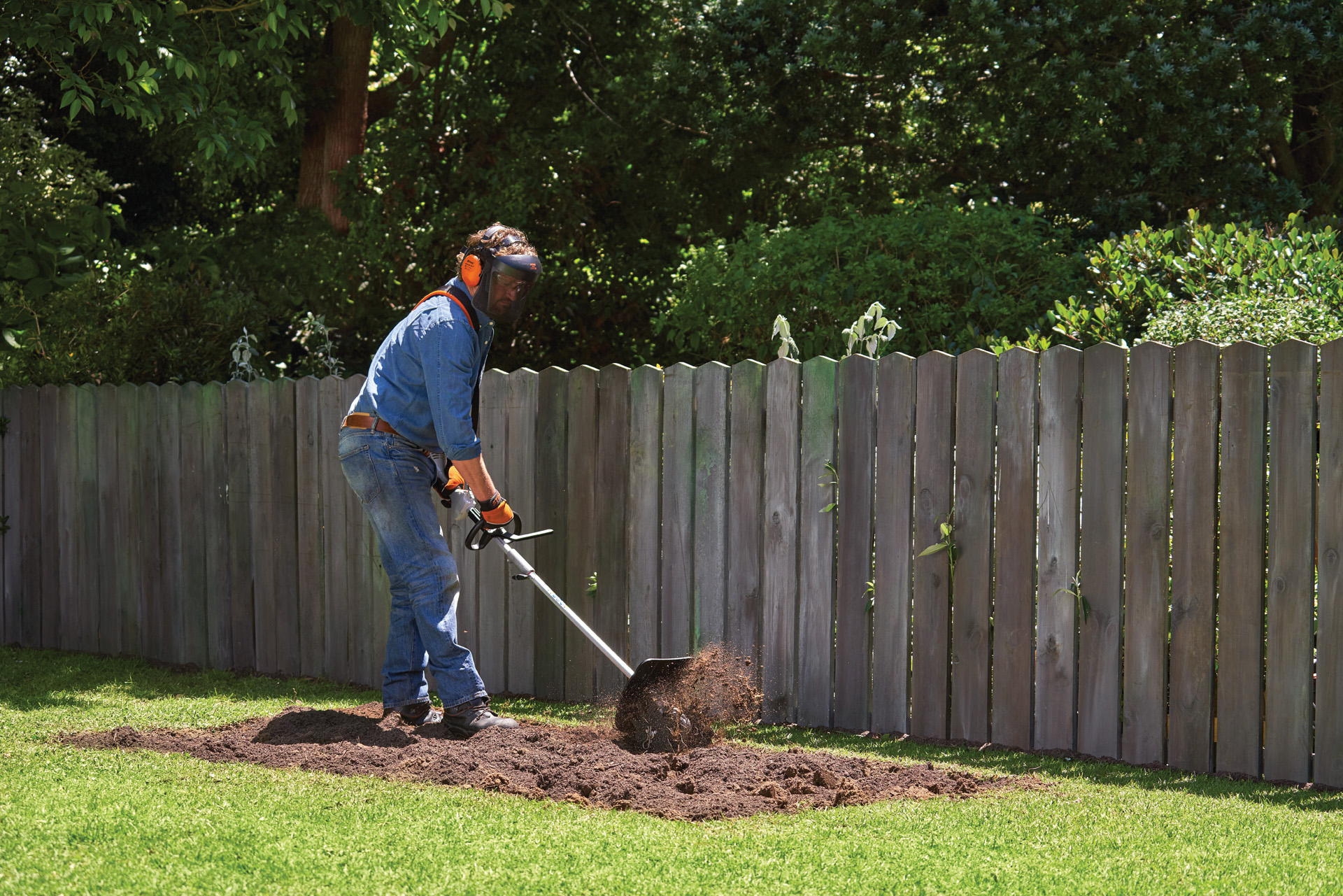 Een persoon met beschermende kleding cultiveert de grond voor een groentebed met een STIHL bodemfrees