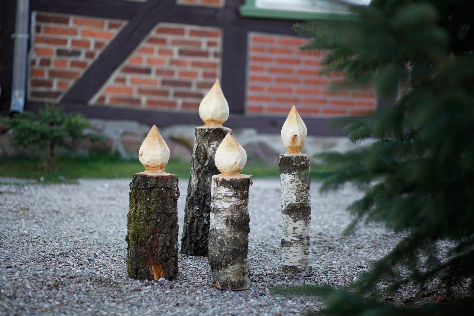 Vier houten doe-het-zelfkaarsen die op een pad naast een spar staan