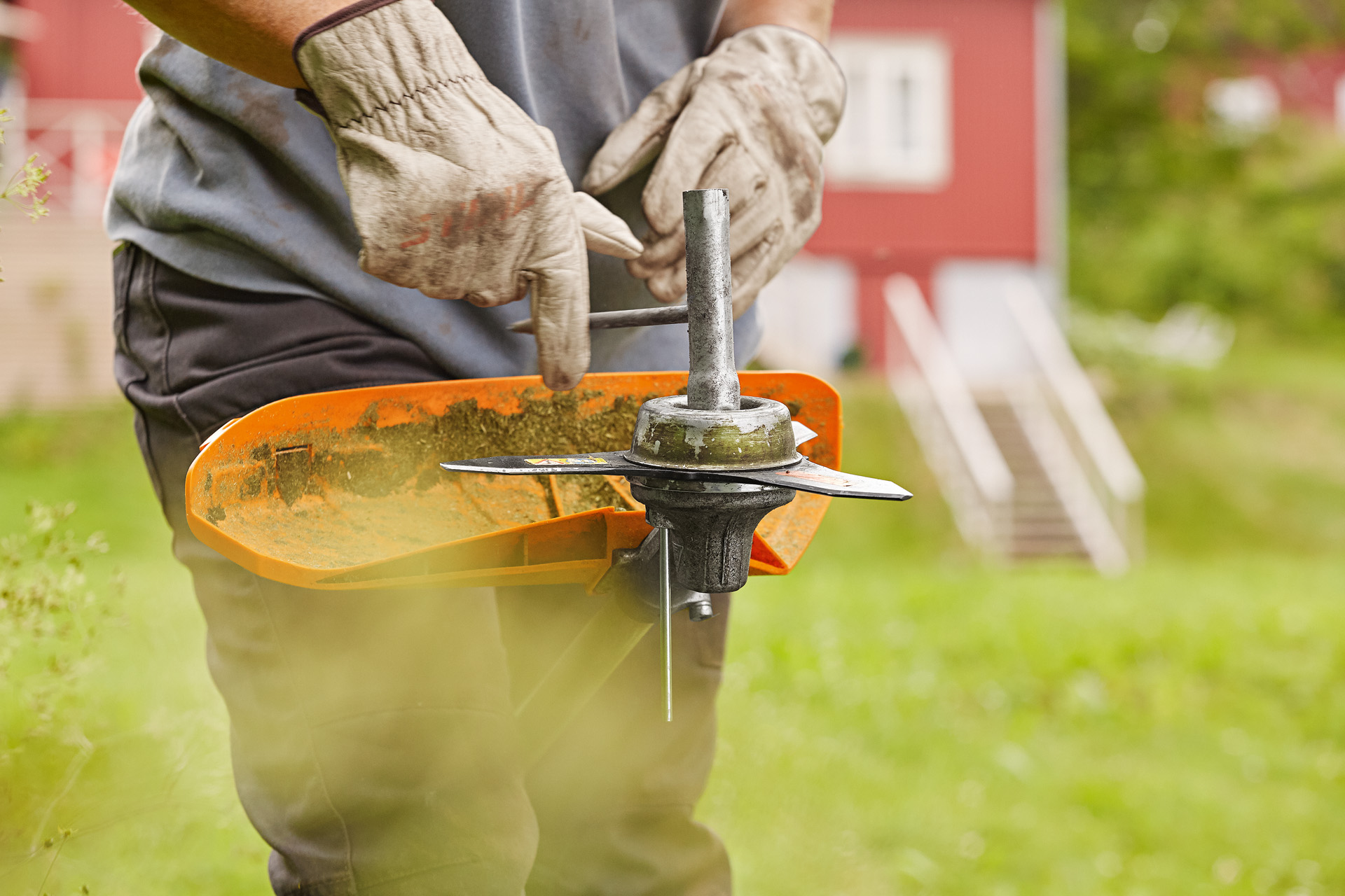 Persoon op groen gazon voor een huis die het grassnijblad van een bosmaaier vervangt