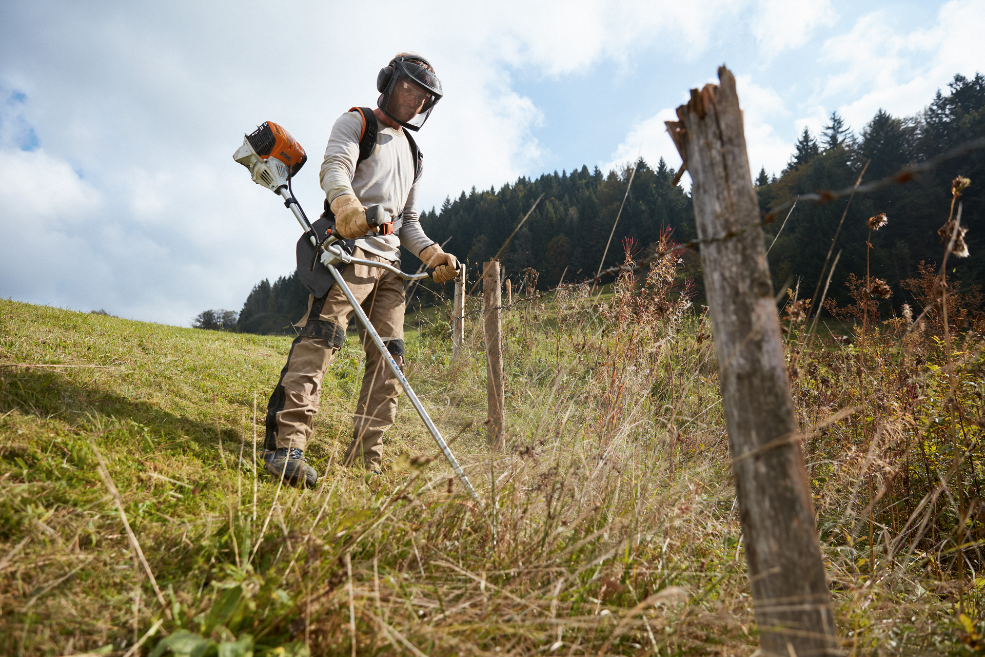 Man in beschermende uitrusting maait gras op helling met een STIHL benzinebosmaaier FS 91