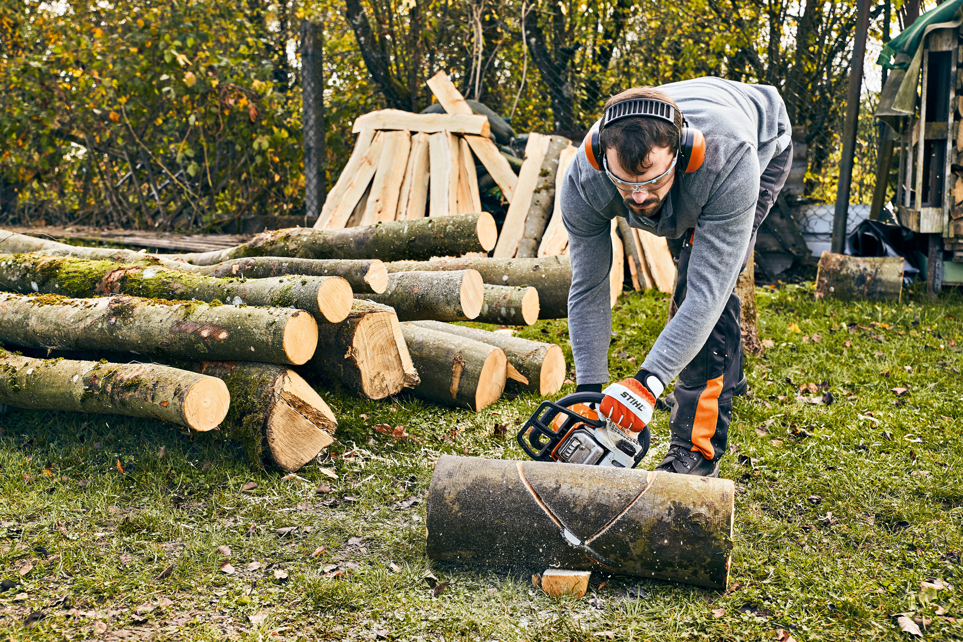 Man met gehoorbescherming en STIHL MS 180 benzinekettingzaag maakt een tuinbank