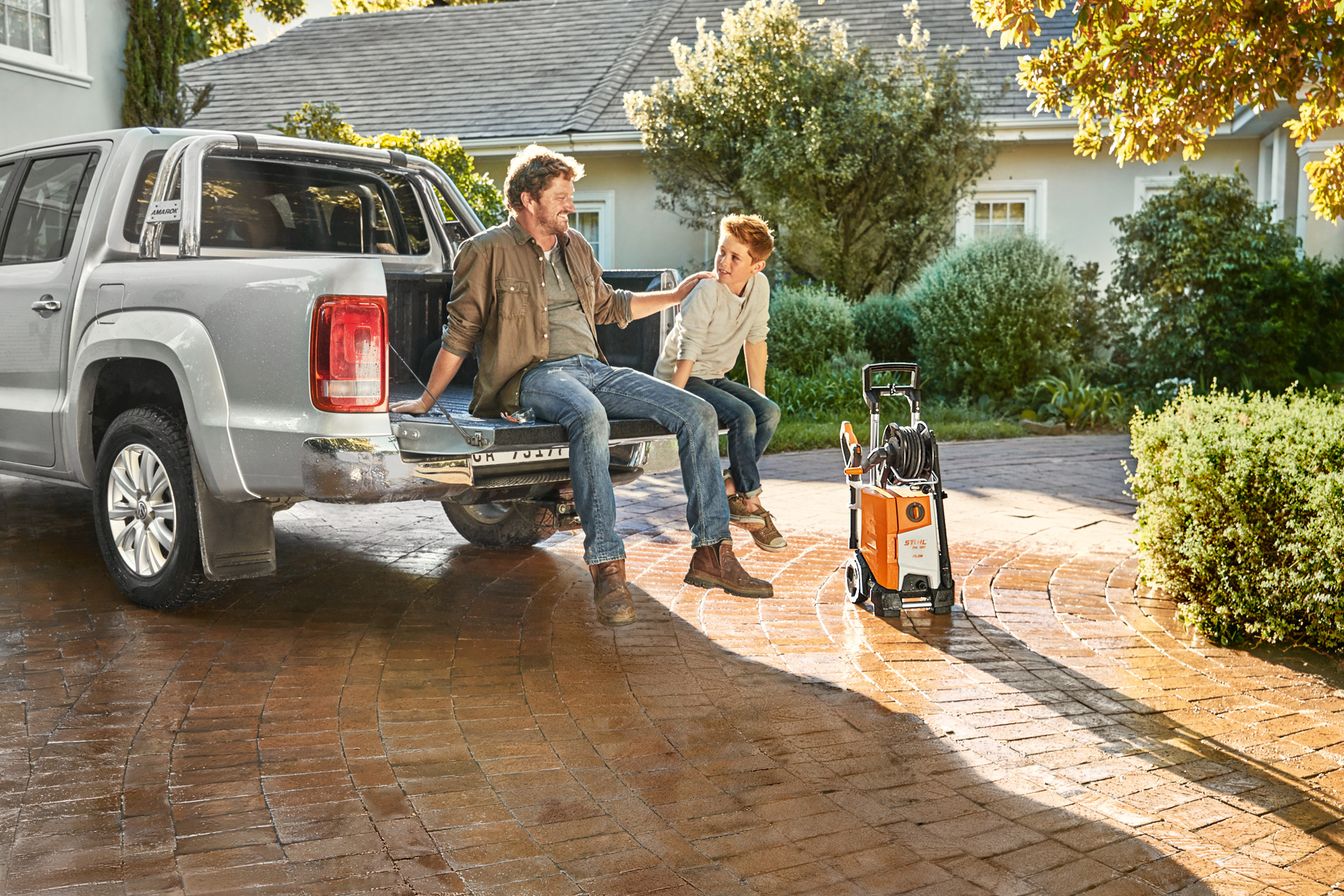 Een man en jongen zitten op de laadvloer van een pick-up met naast het voertuig een STIHL RE 130 plus hogedrukreiniger