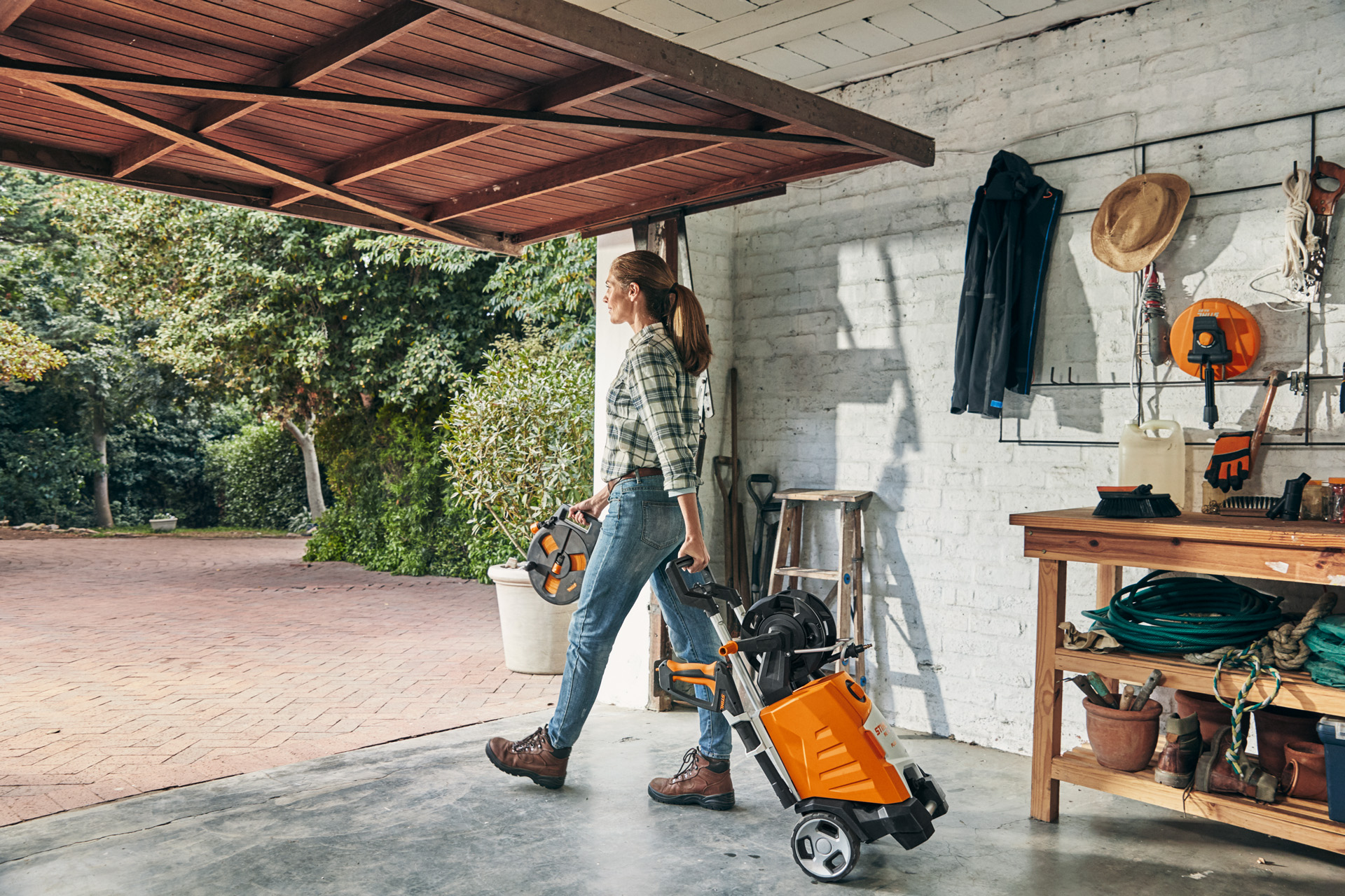 Een vrouw verlaat een garage met de STIHL hogedrukreiniger RE 130 PLUS om deze te gebruiken