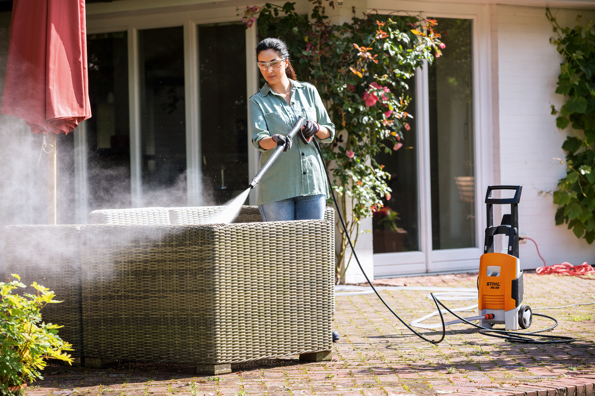 Vrouw met veiligheidsbril reinigt haar tuinmeubelen op het terras met de STIHL RE 88 hogedrukreiniger.