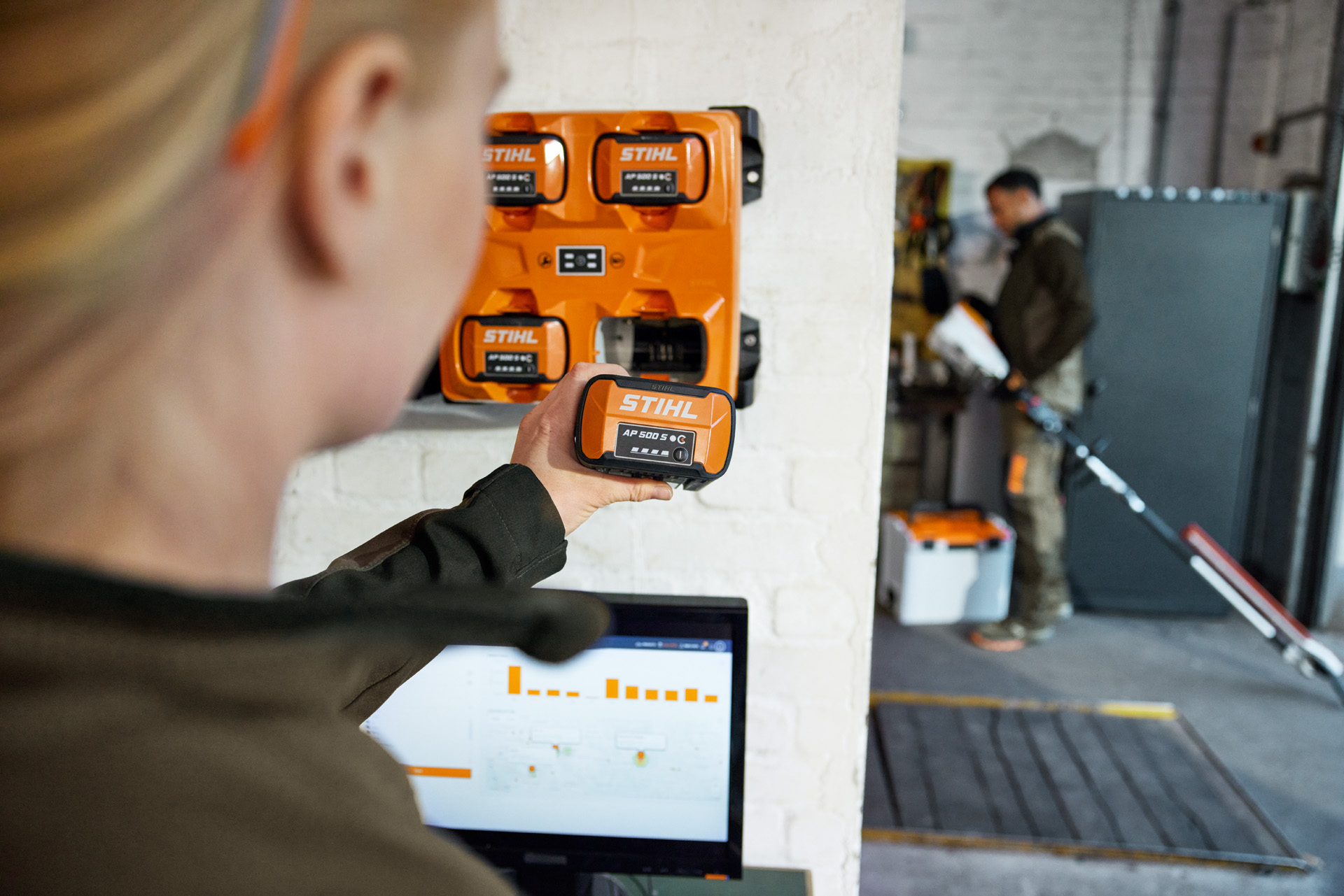 Een vrouw voor een laptop neemt een AP 300 S uit de STIHL AL 301-4 multilader