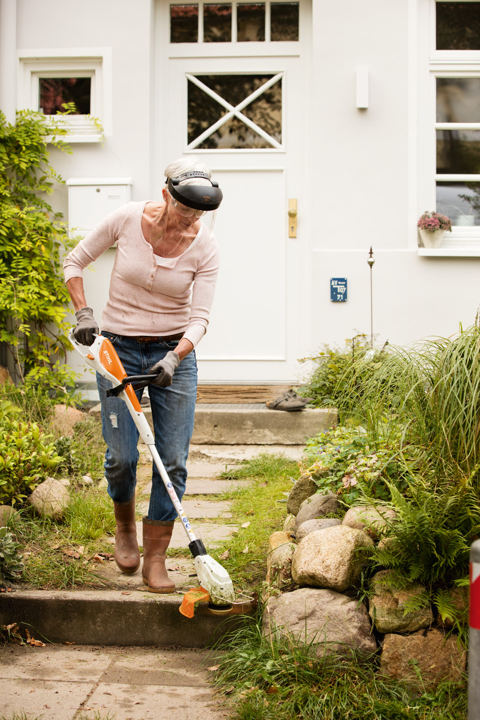 Vrouw met veiligheidsbril trimt graskanten op een niveau voor een huis met de STIHL accukantenmaaier FSA 45