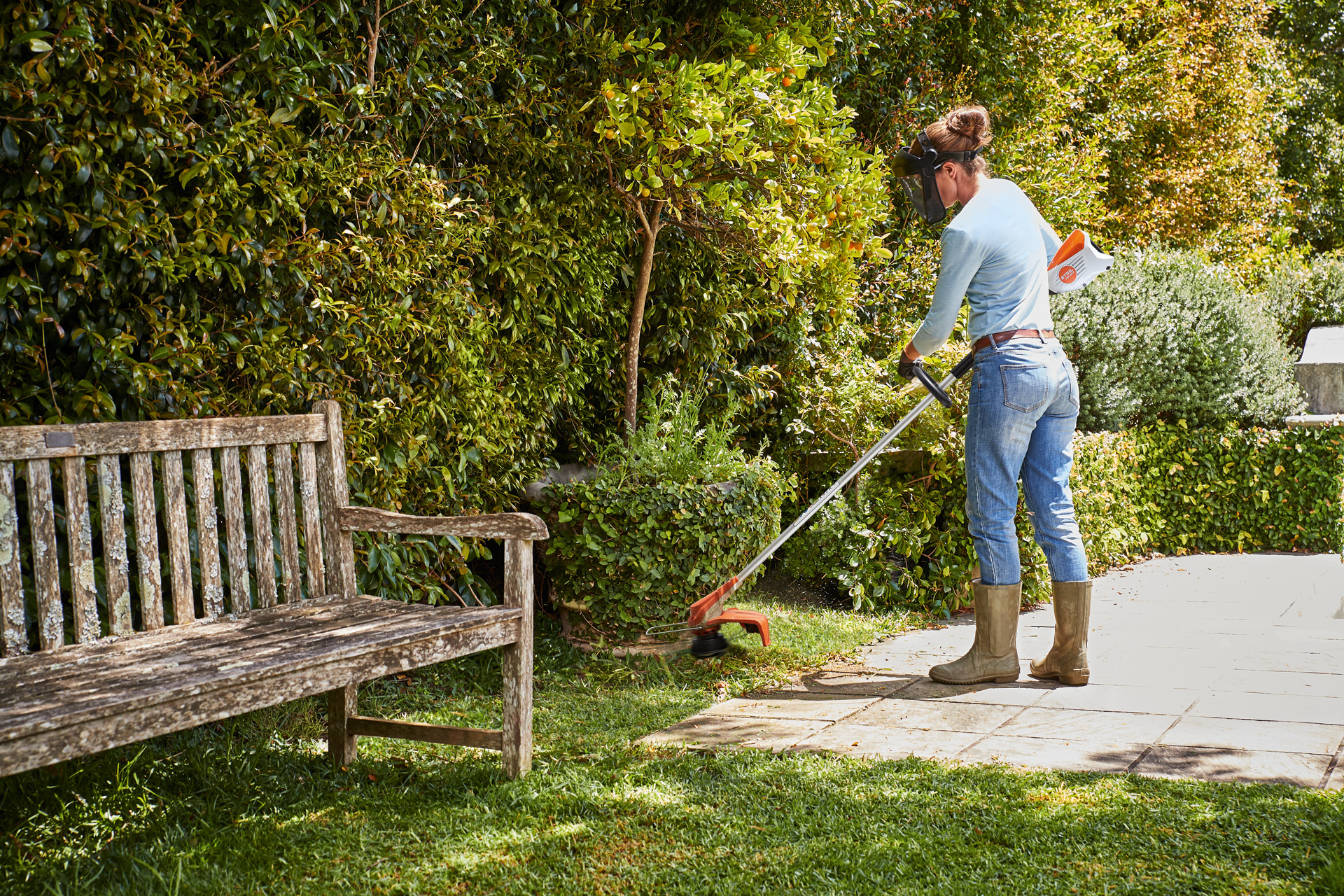 Een vrouw maait gras rond een kleine boom met een STIHL FSA 60 R accugrastrimmer