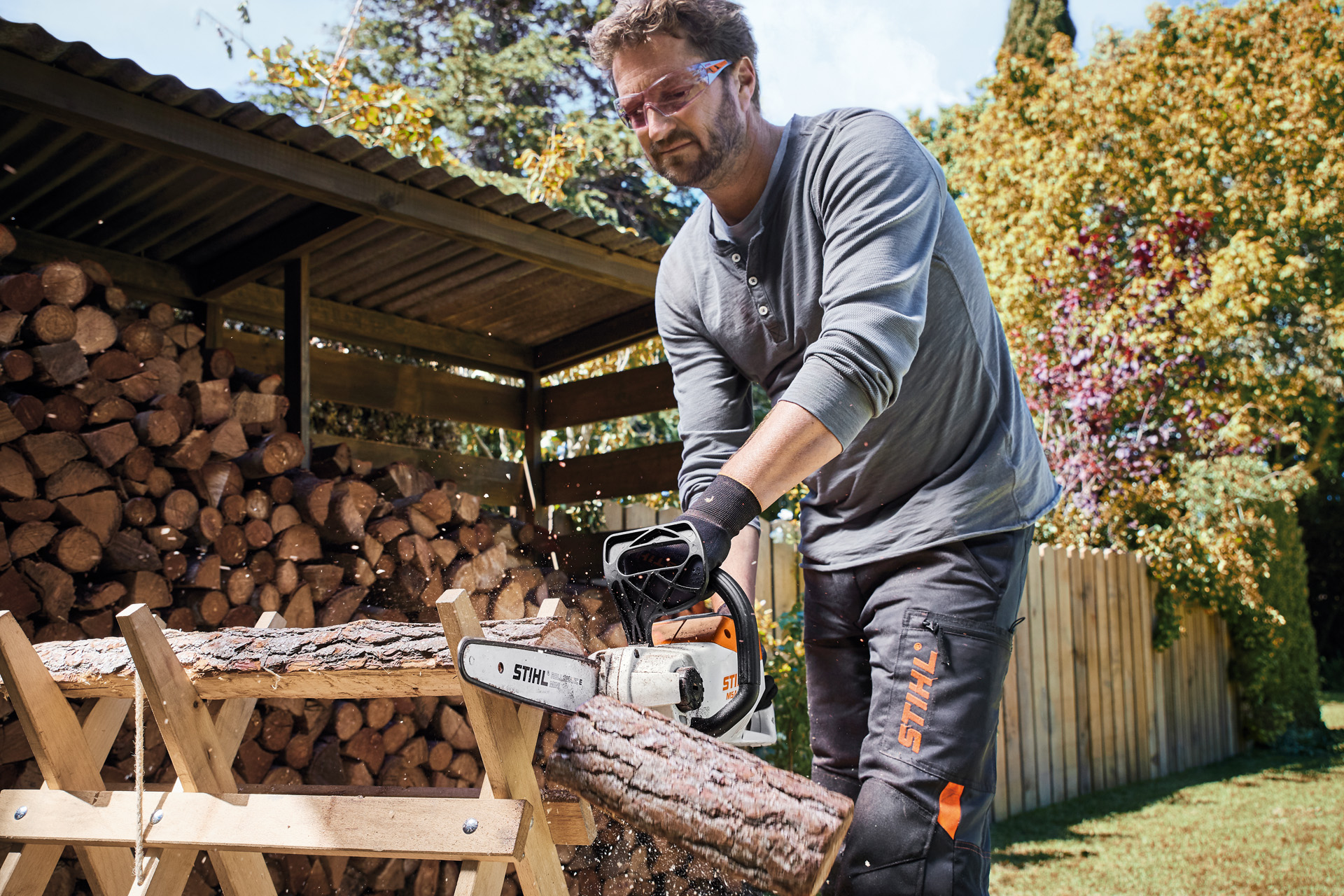 Een man met een veiligheidsbril op zaagt door een houtblok met een STIHL MSA 140 C-B accukettingzaag