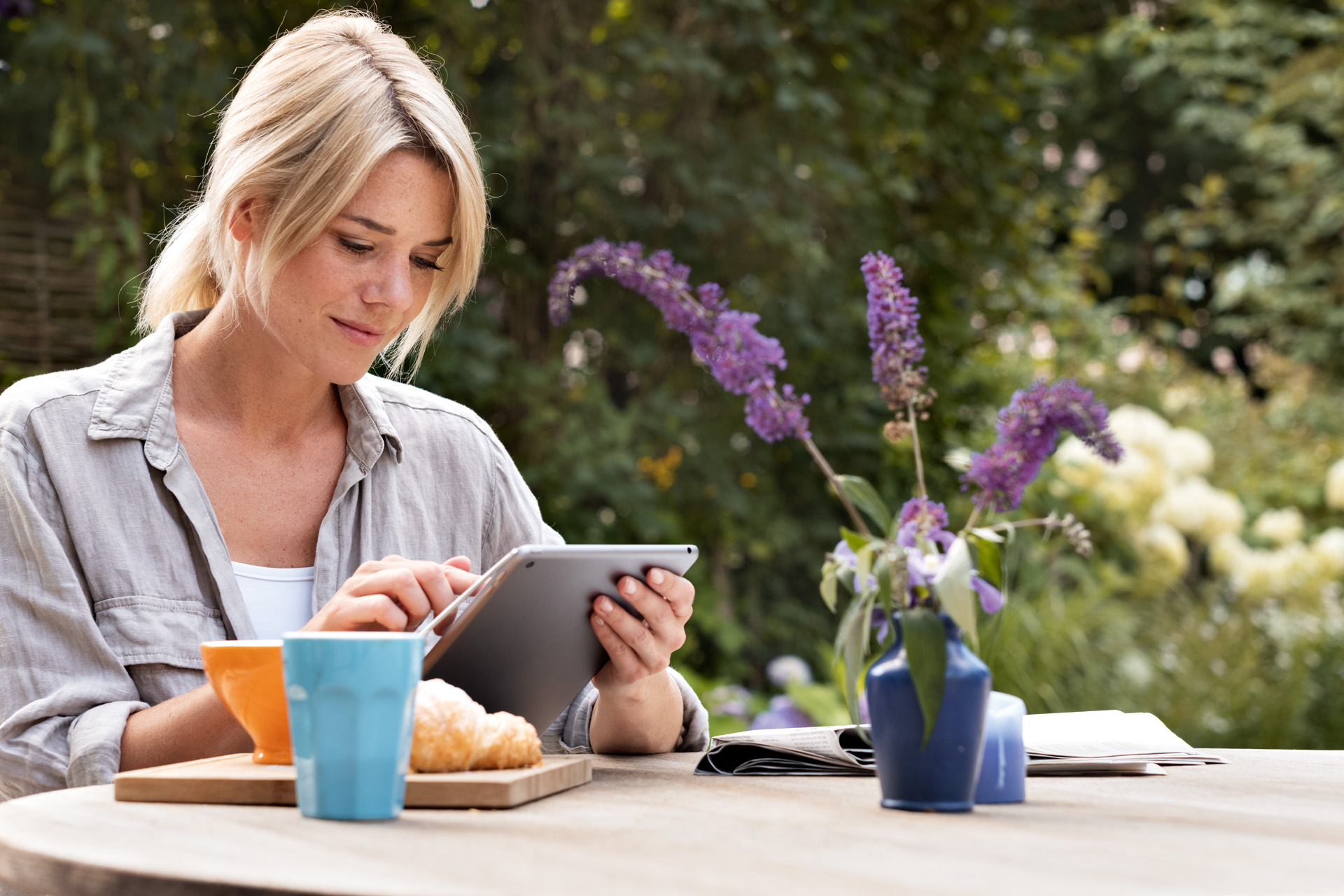 Vrouw werkt op tablet aan ontbijttafel in de tuin