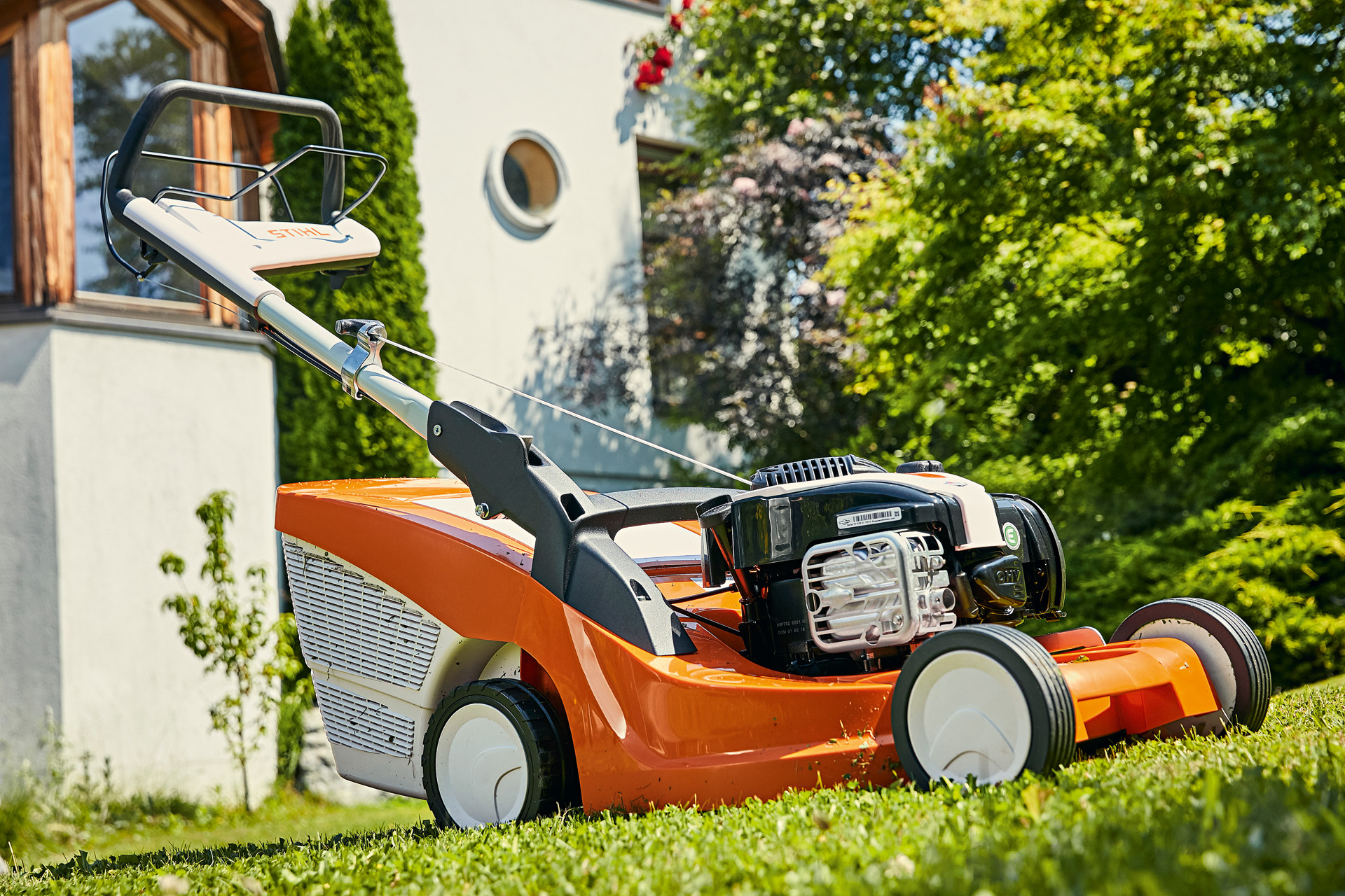 A STIHL RM 443 T petrol lawn mower in a garden with a house in the background