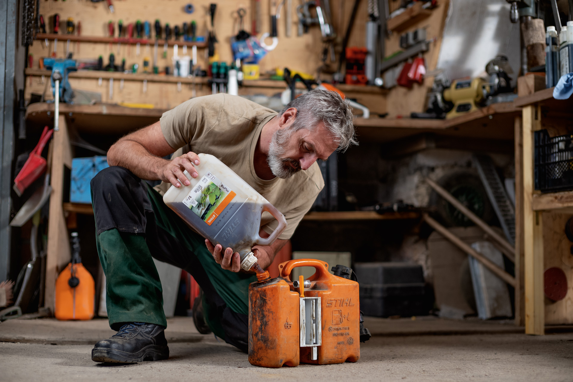 Man zit geknield op de grond in een werkplaats en giet STIHL brandstof in een oranje jerrycan