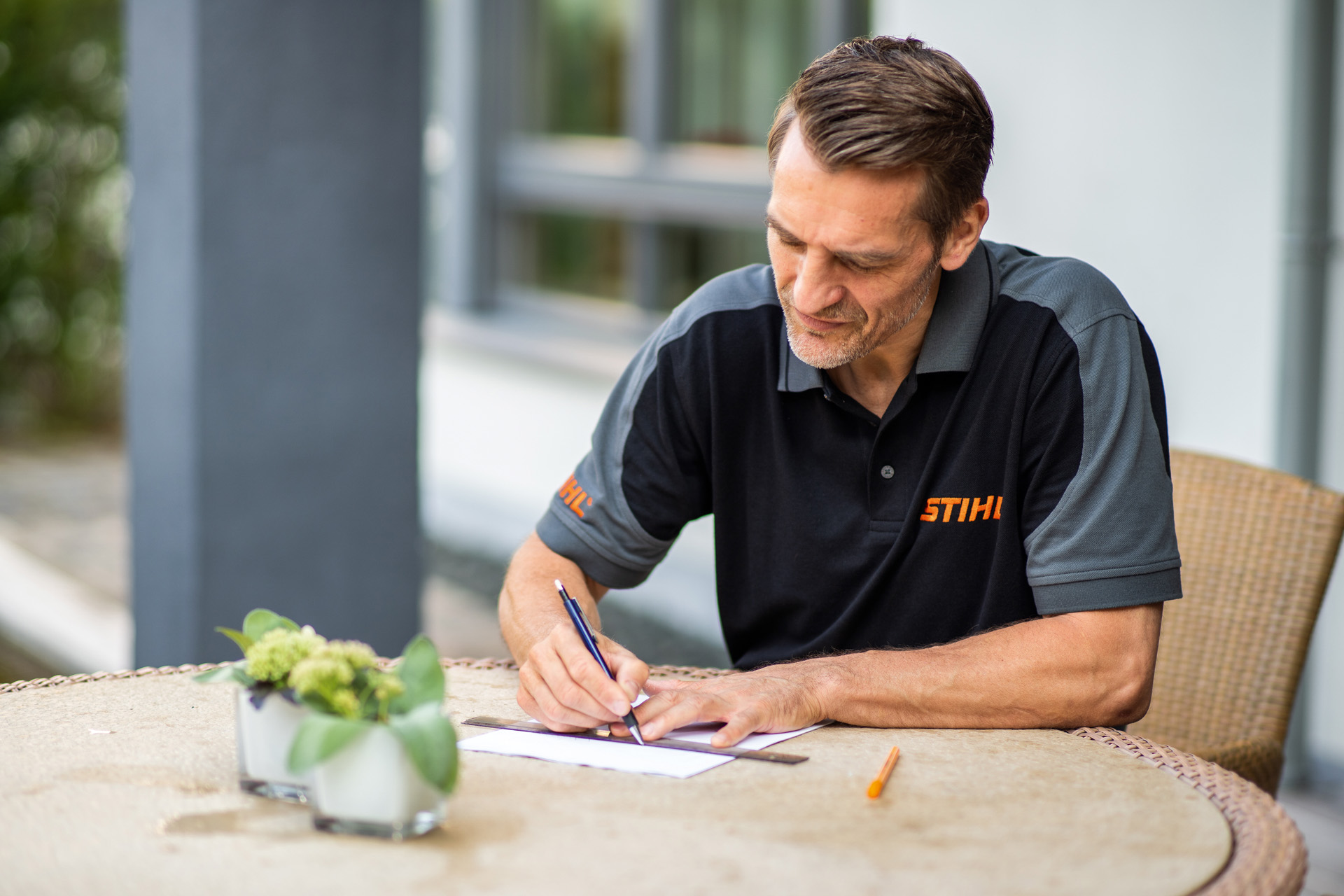 STIHL dealer zit aan de tuintafel en tekent het plan van het gazon dat de robotmaaier iMOW moet maaien