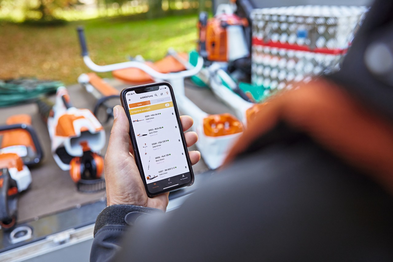 Iemand met een smartphone waarop de STIHL connected App geopend is. Op de achtergrond diverse STIHL machines.