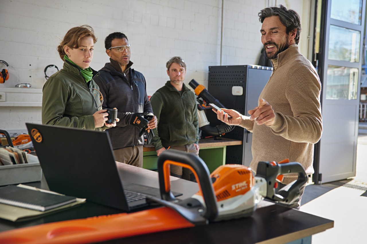 Een team landschapsarchitecten bespreekt zijn werk in een magazijn met behulp van de STIHL connected app op hun smartphone.