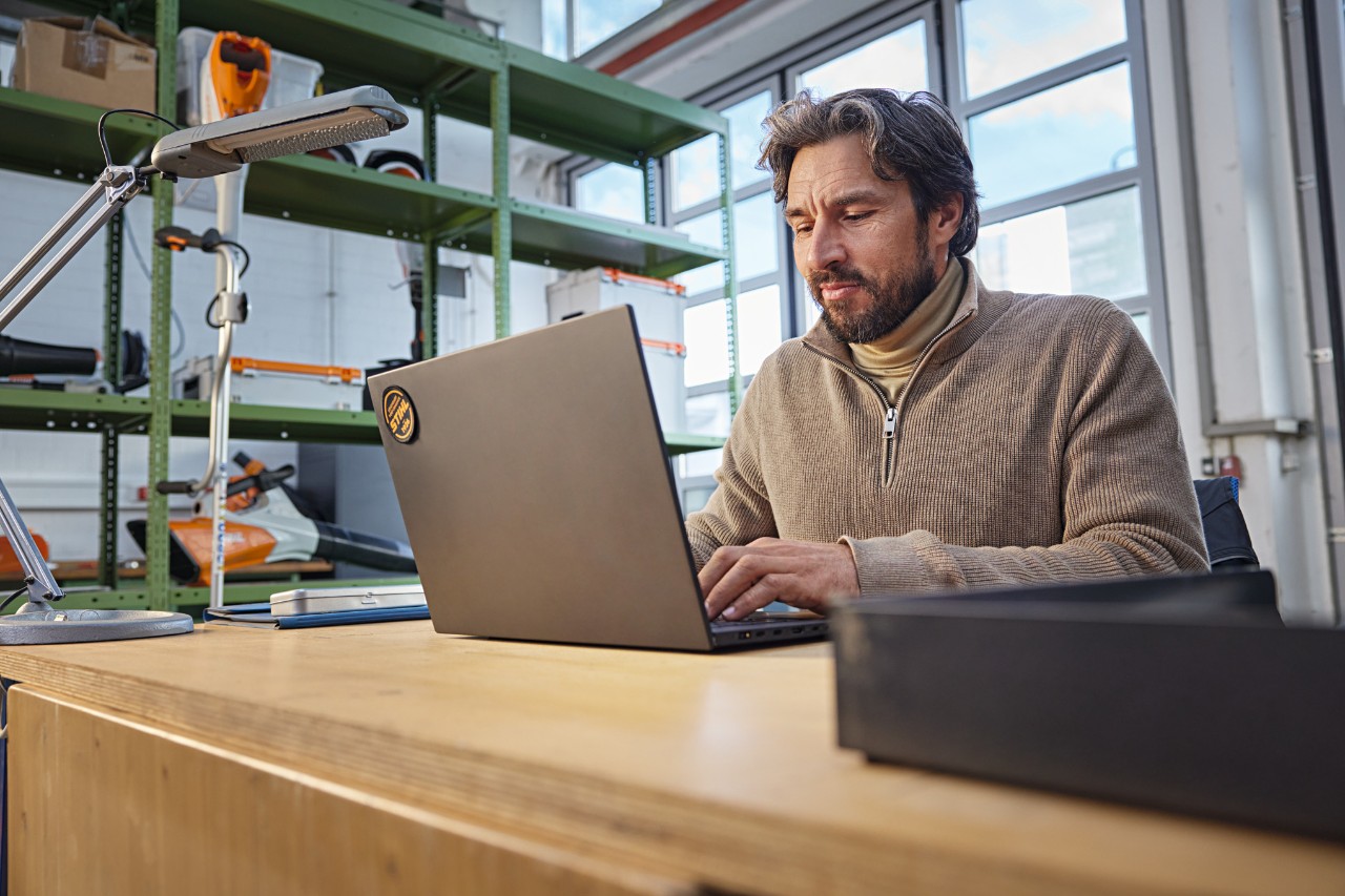 Iemand zit met een laptop aan een bureau in een werkplaats.