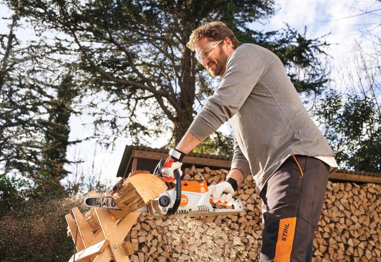 Een man die de STIHL MSA 70 gebruikt om hout in de tuin te zagen