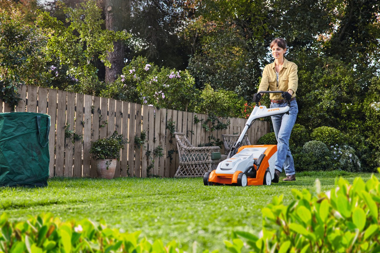 Man bij het grasmaaien met STIHL benzinegrasmaaier RM 448 TC naast een houten hek