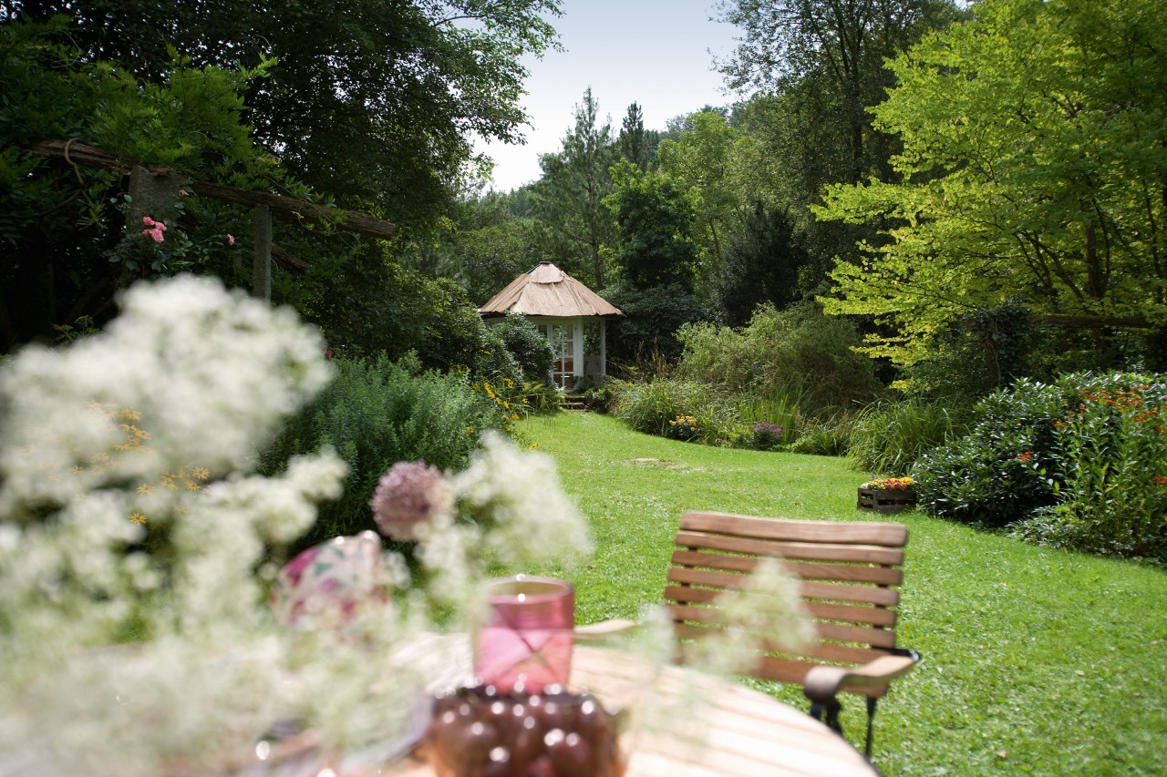 Een groen gazon na het verticuteren met op de voorgrond een tuintafel en op de achtergrond een tuinhuisje