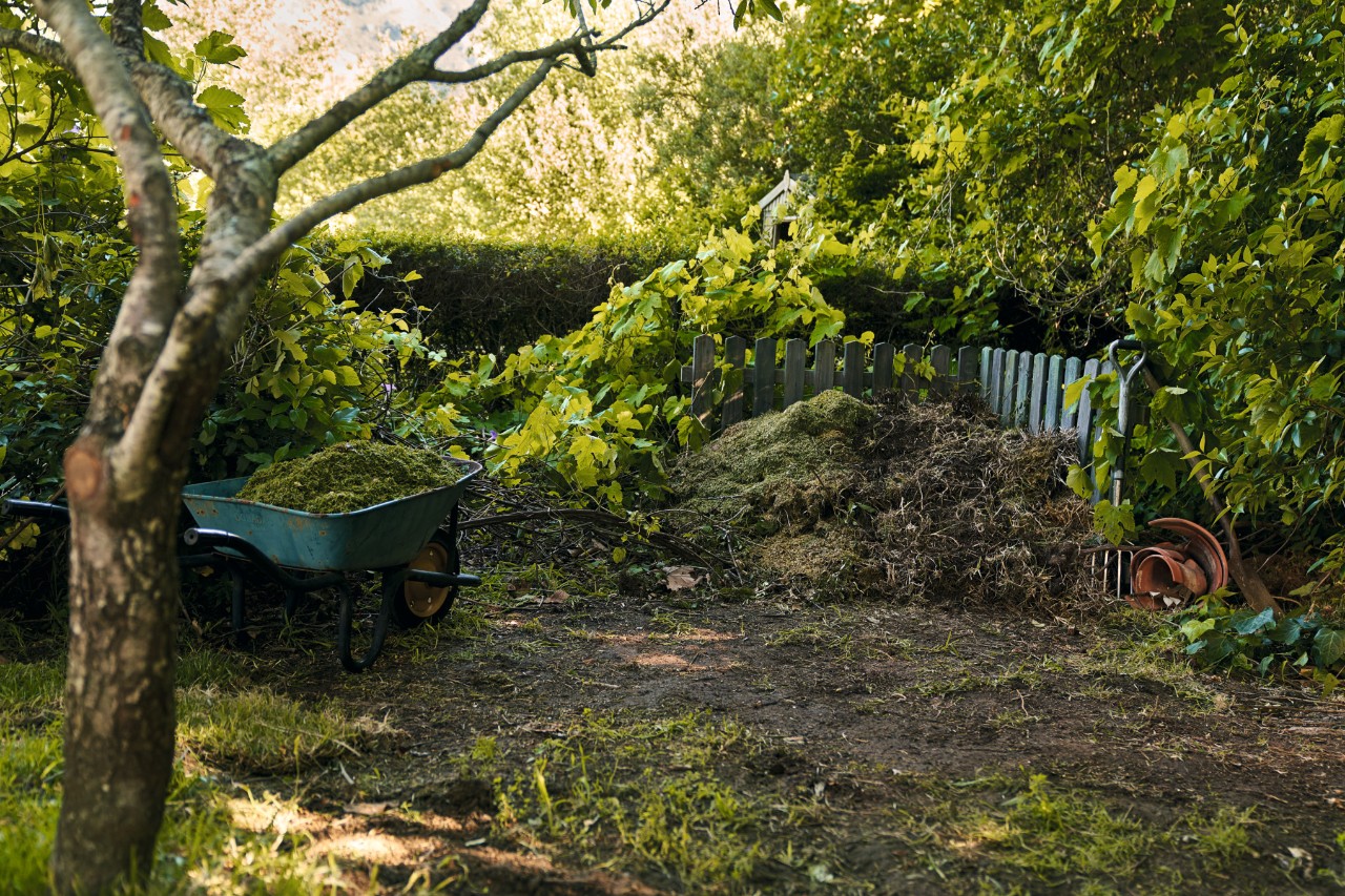 Kruiwagen met tuinafval naast composthoop voor een heg